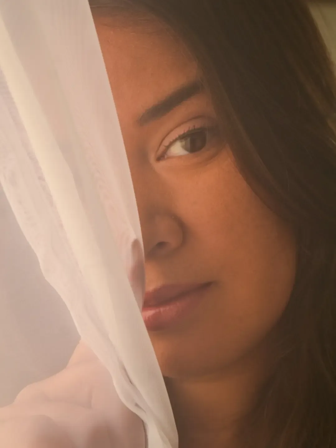 Retrato de mulher com parte do rosto vista através de tecido branco translúcido.