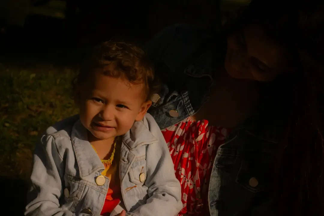 Criança sorrindo, de roupa cinza com detalhe vermelho, iluminada pelo sol.