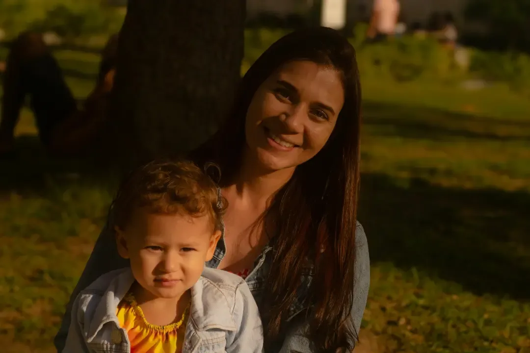 Mulher e criança sentadas juntas ao ar livre, iluminadas pelo sol.